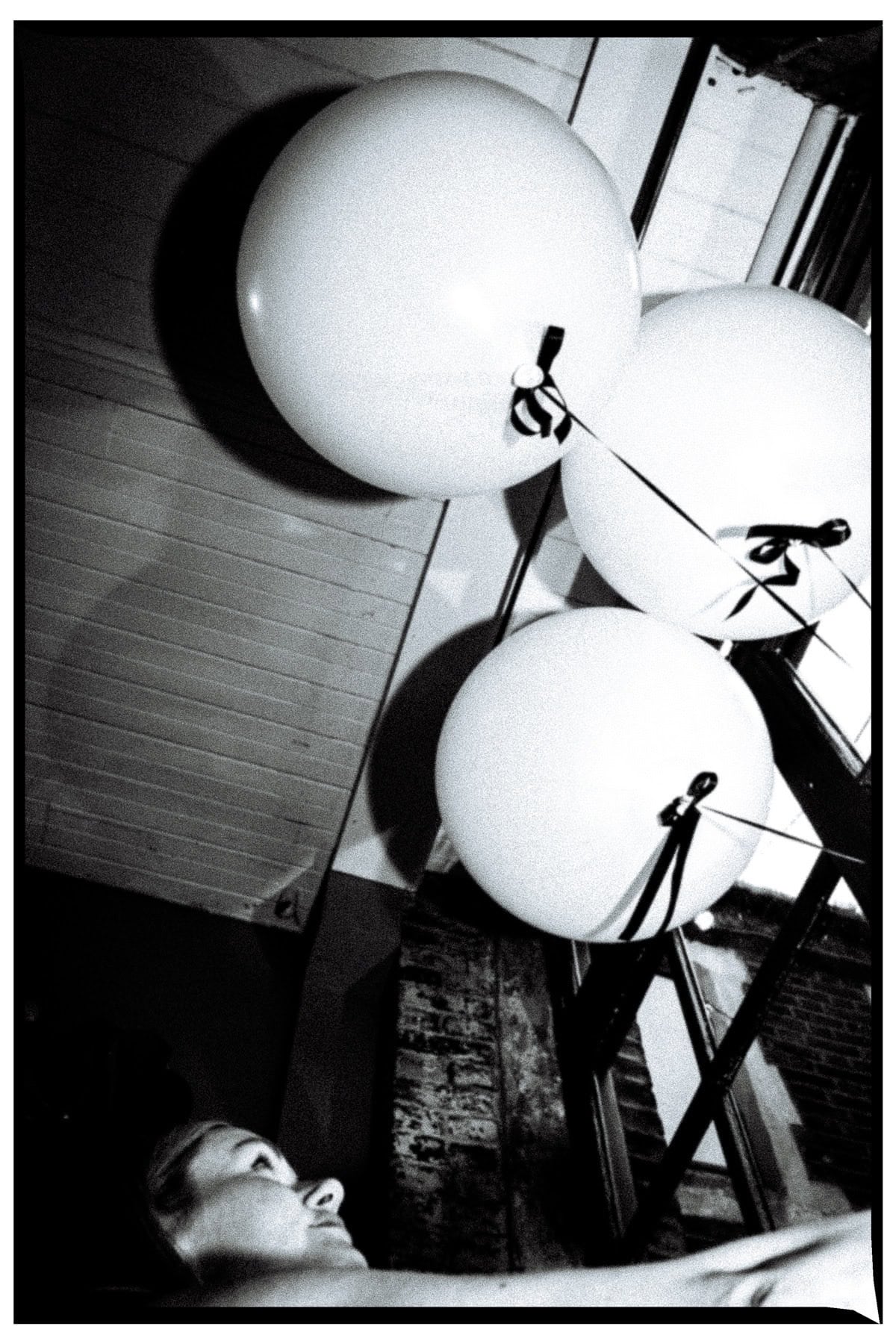 White balloons and a face at the edge of a sharply angled black-and-white frame