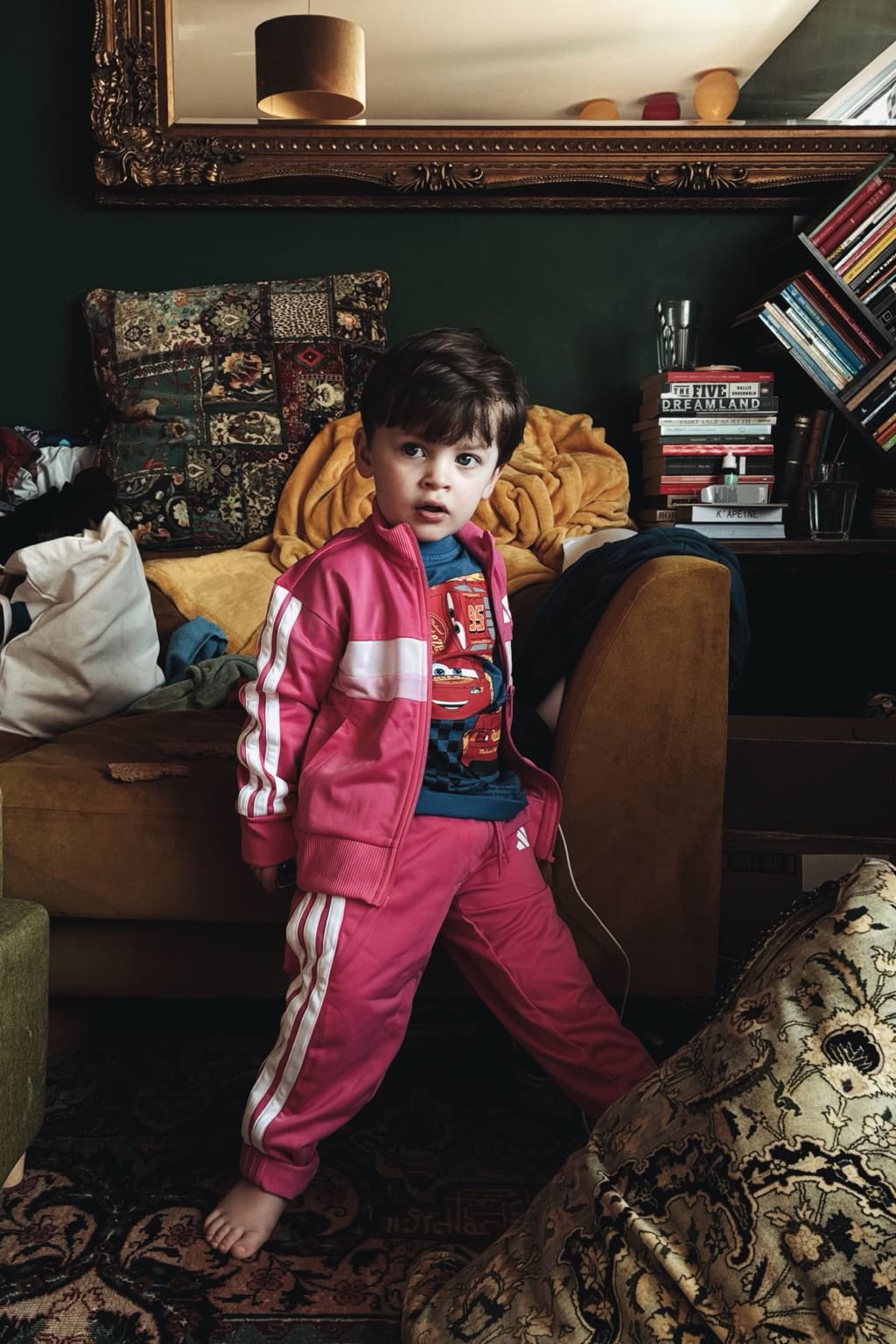 A child in a vivid pink outfit stands in a lived-in room