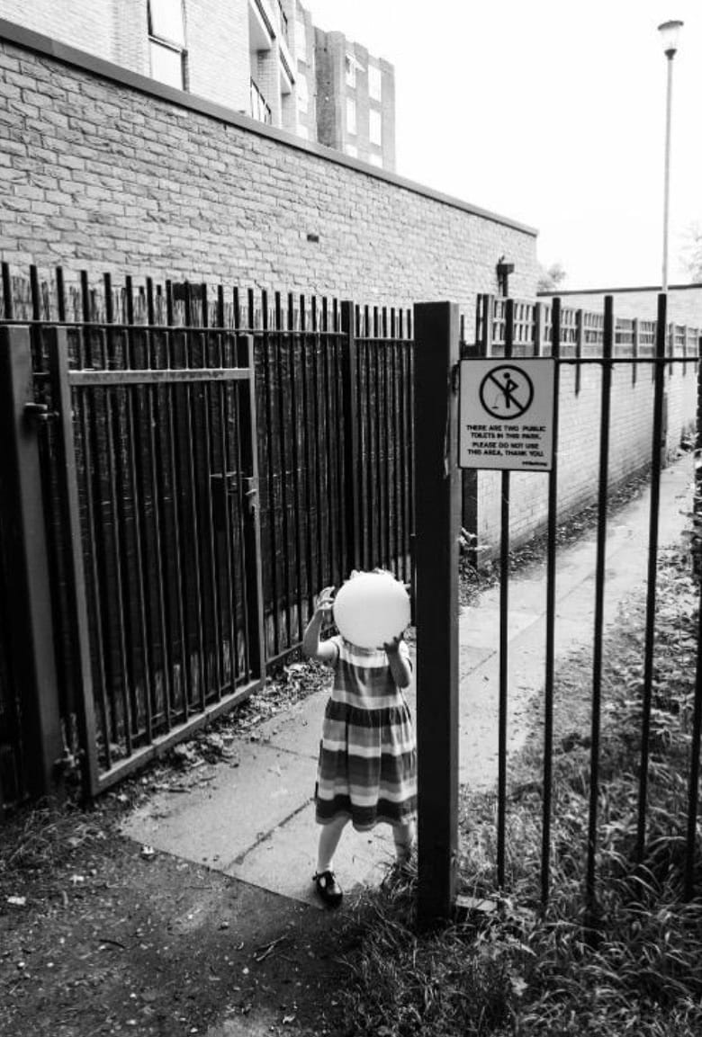 A child carries a balloon past an iron gate