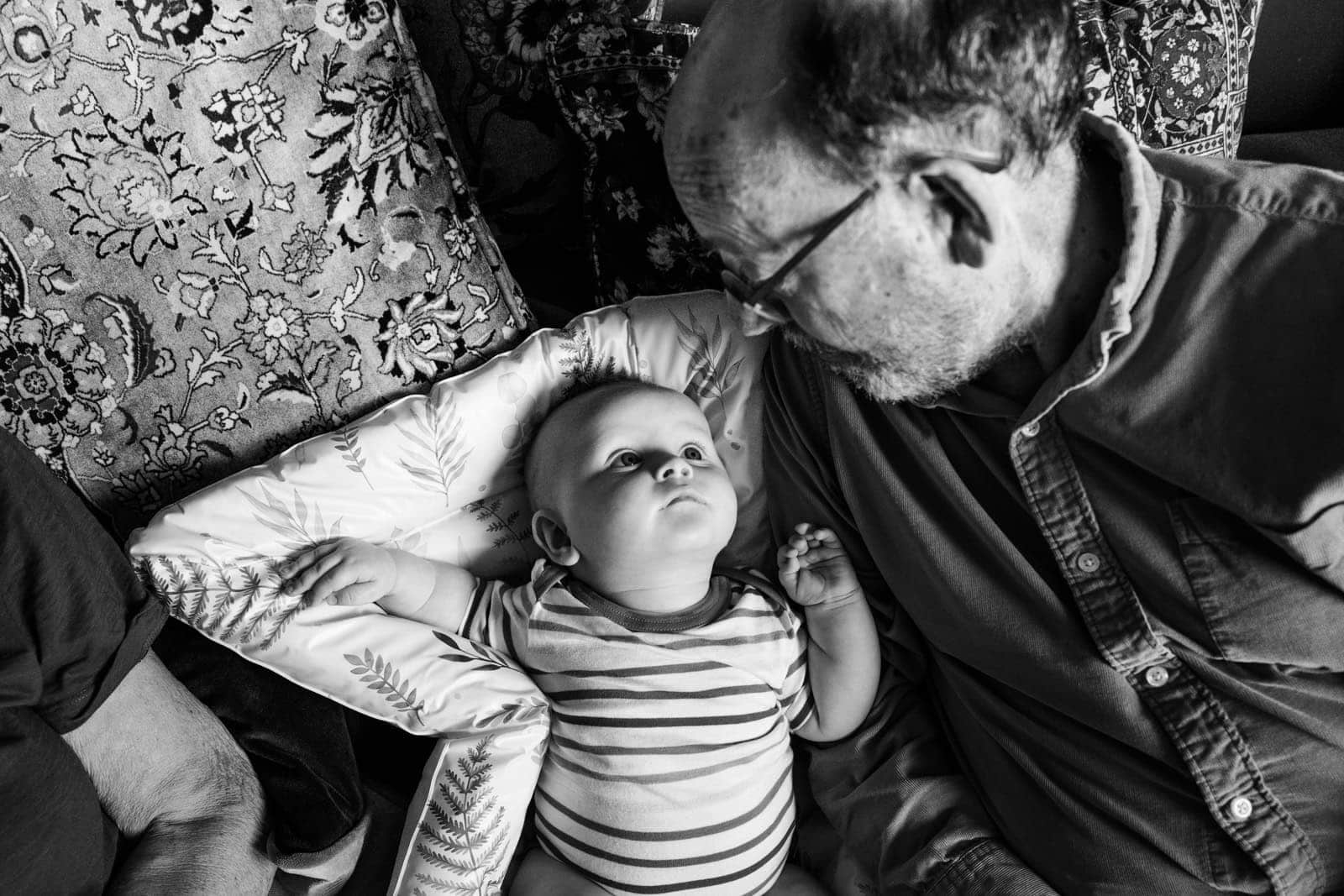 A grandfather leans over a young child resting on a patterned sofa