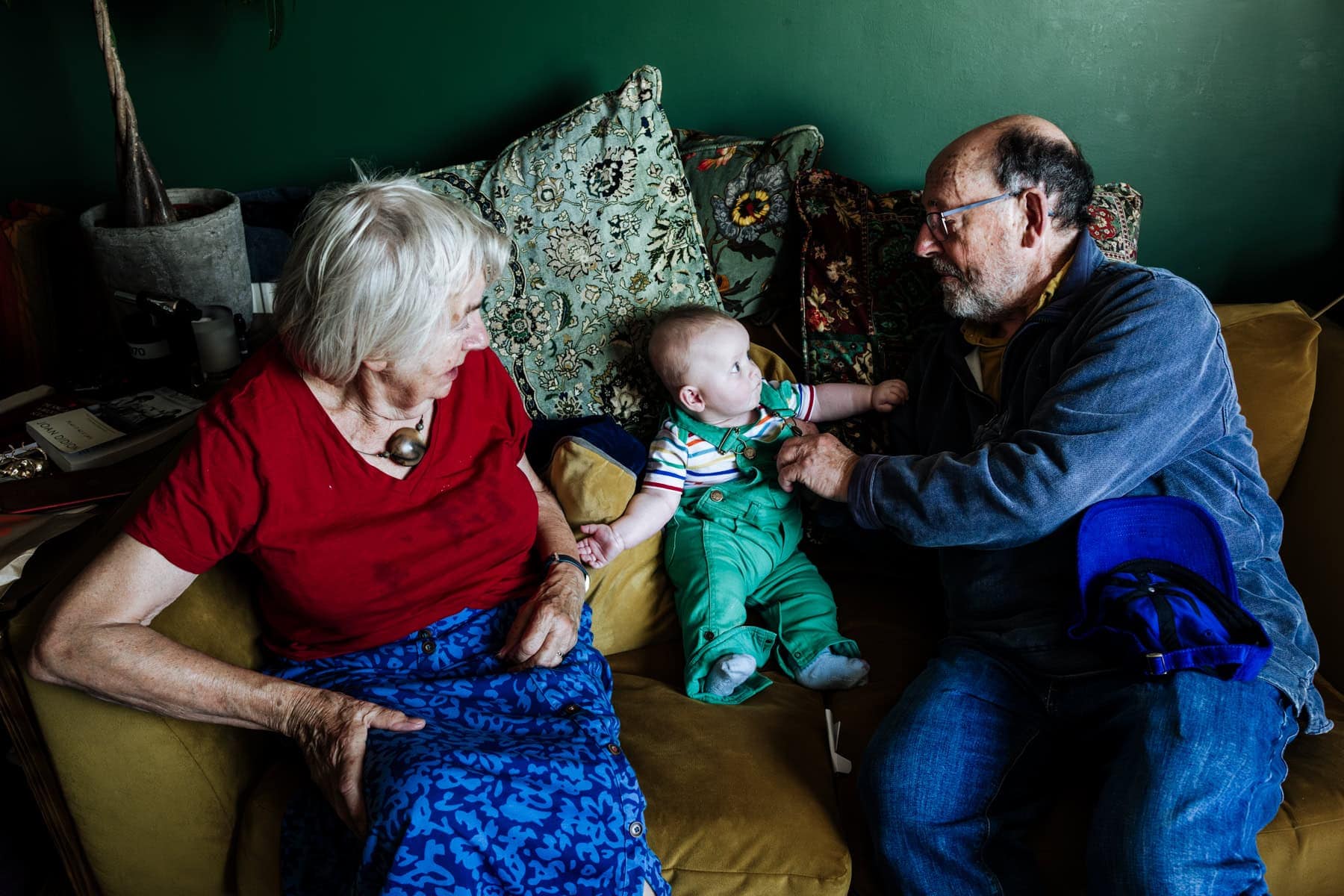 Grandparents sit with their young grandchild on a green sofa