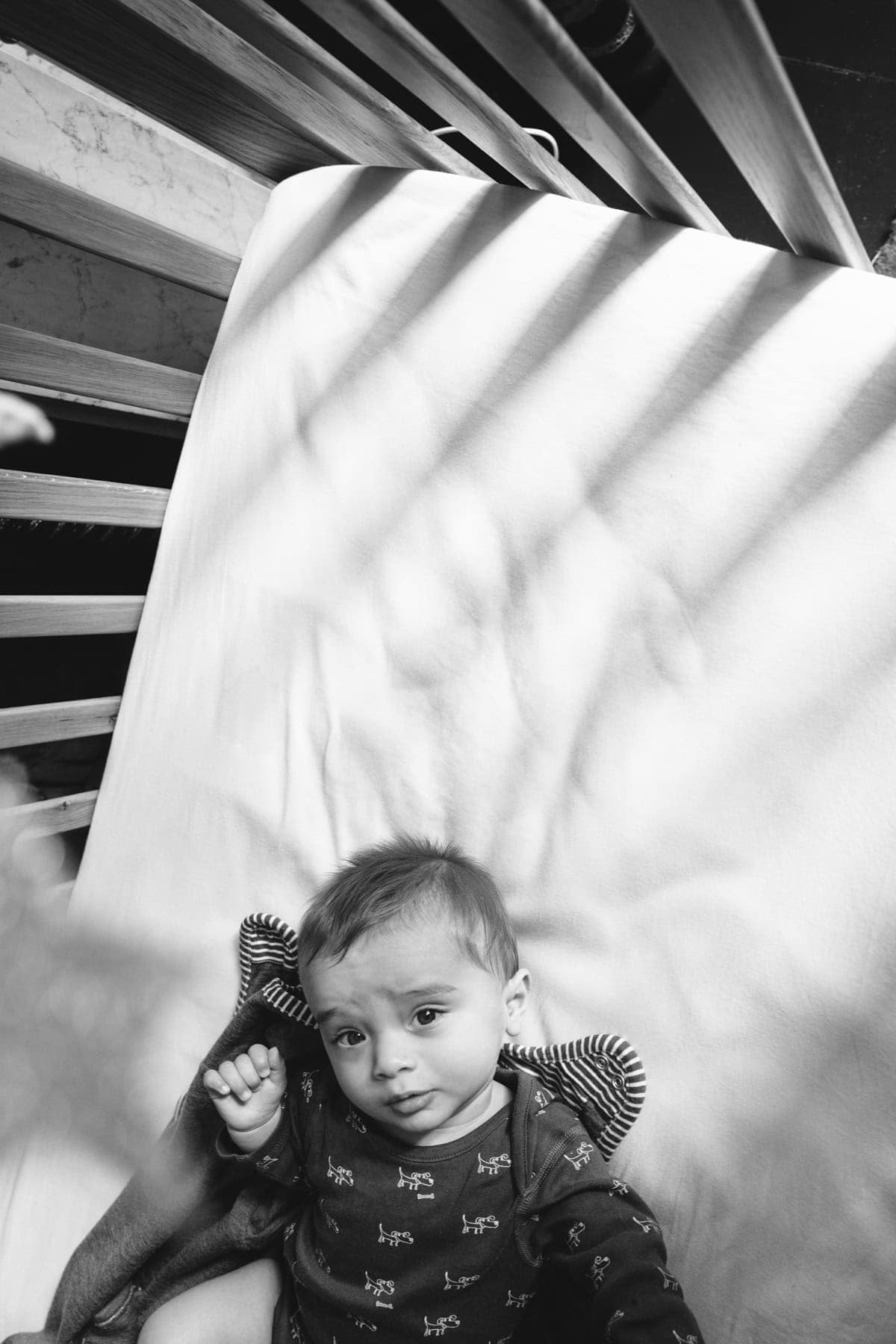 A baby lies beneath slanting shadows in a black-and-white photograph