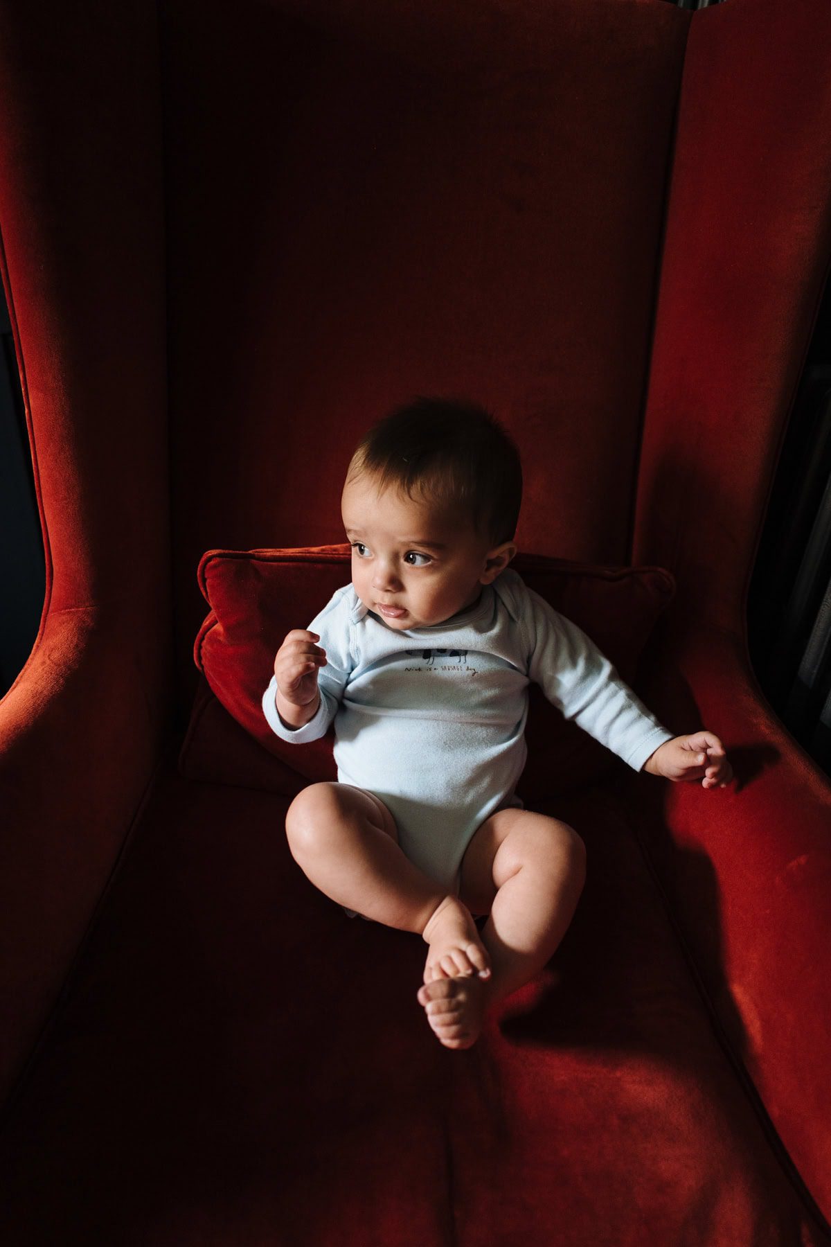 A baby in a red room looks down at a toy