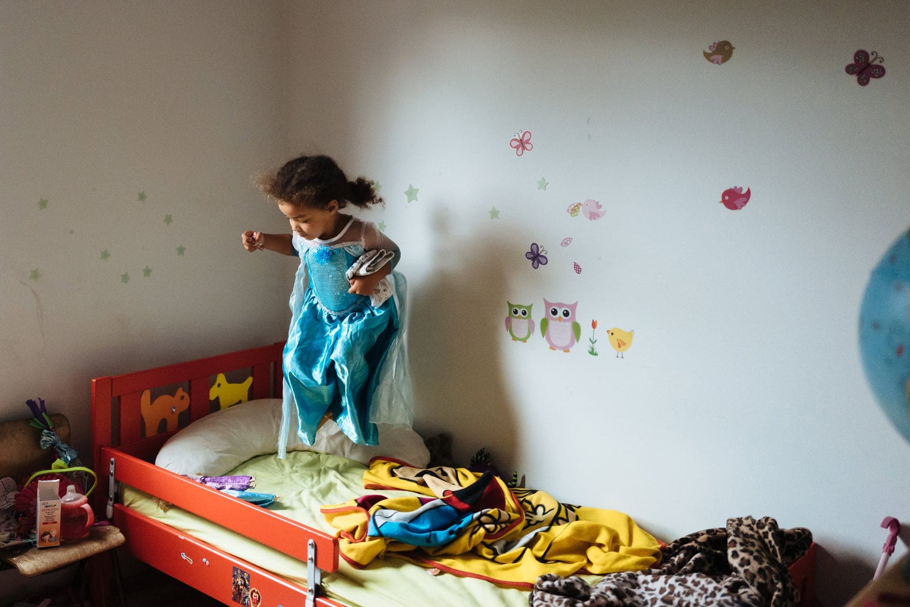 A girl in blue jumps on a bed in a busy room