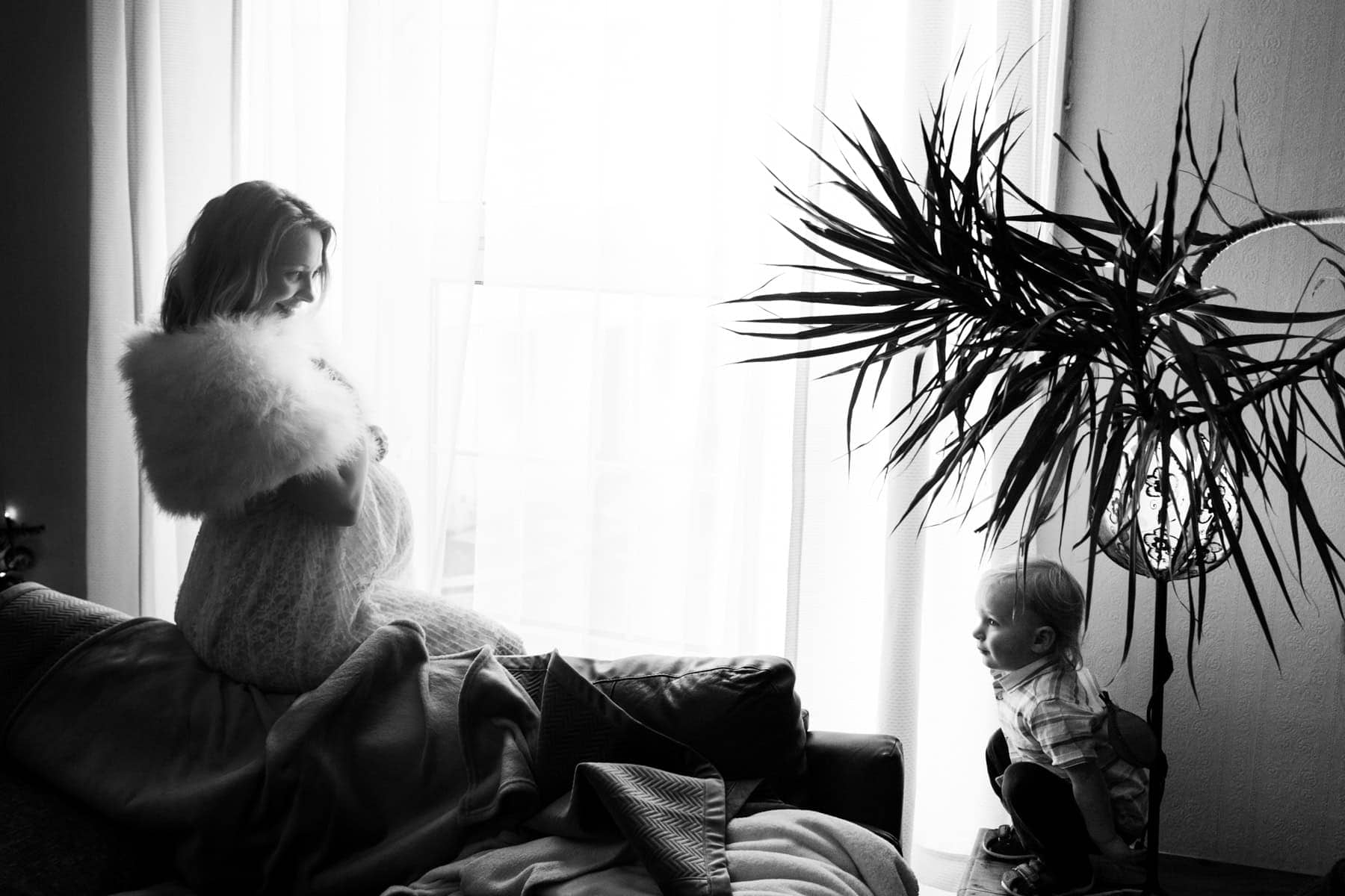 A pregnant woman looks out from a window while a child sits nearby