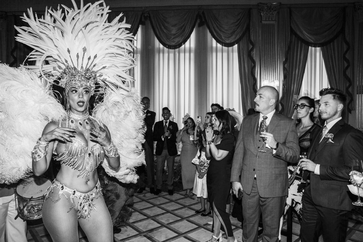 A performer in a feathered headdress stands among wedding guests