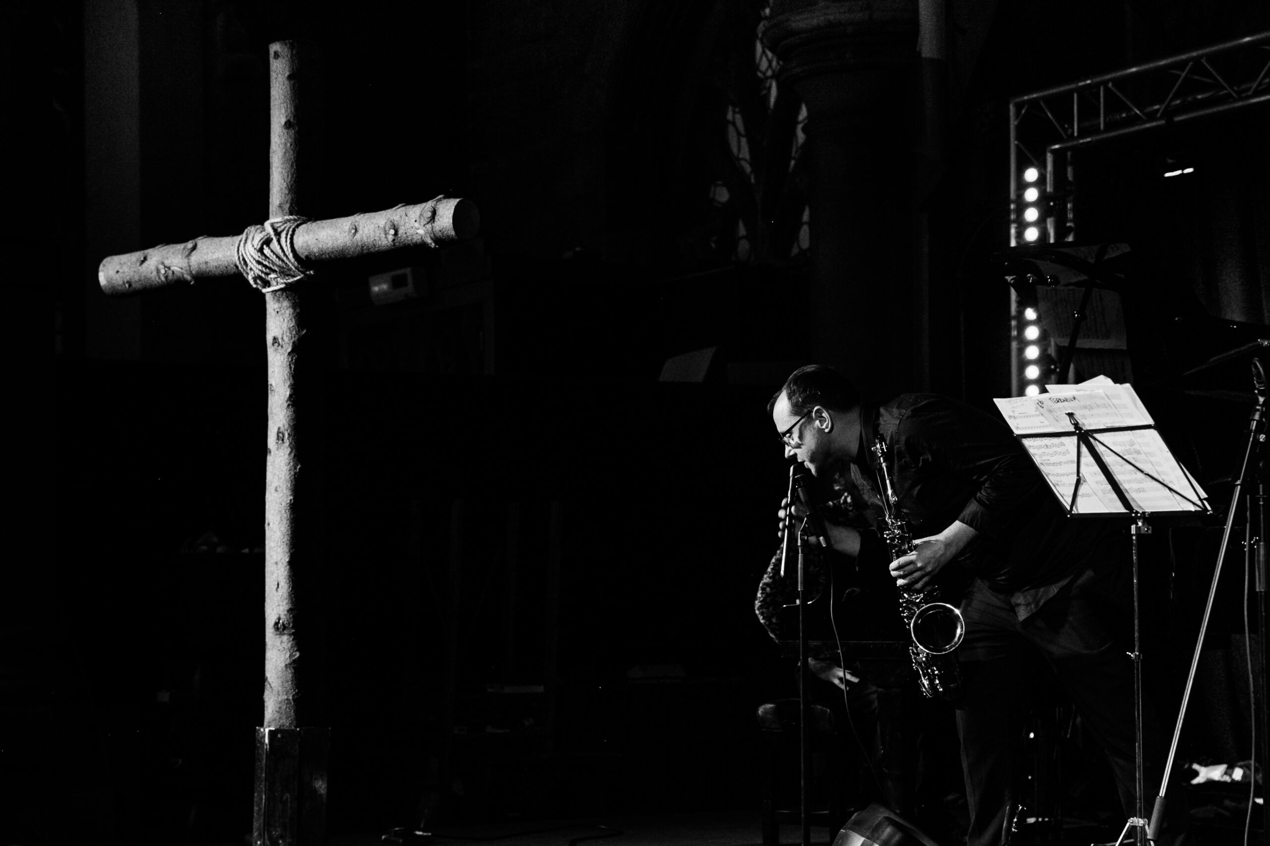 A saxophonist performs beside a wooden cross in a dark venue