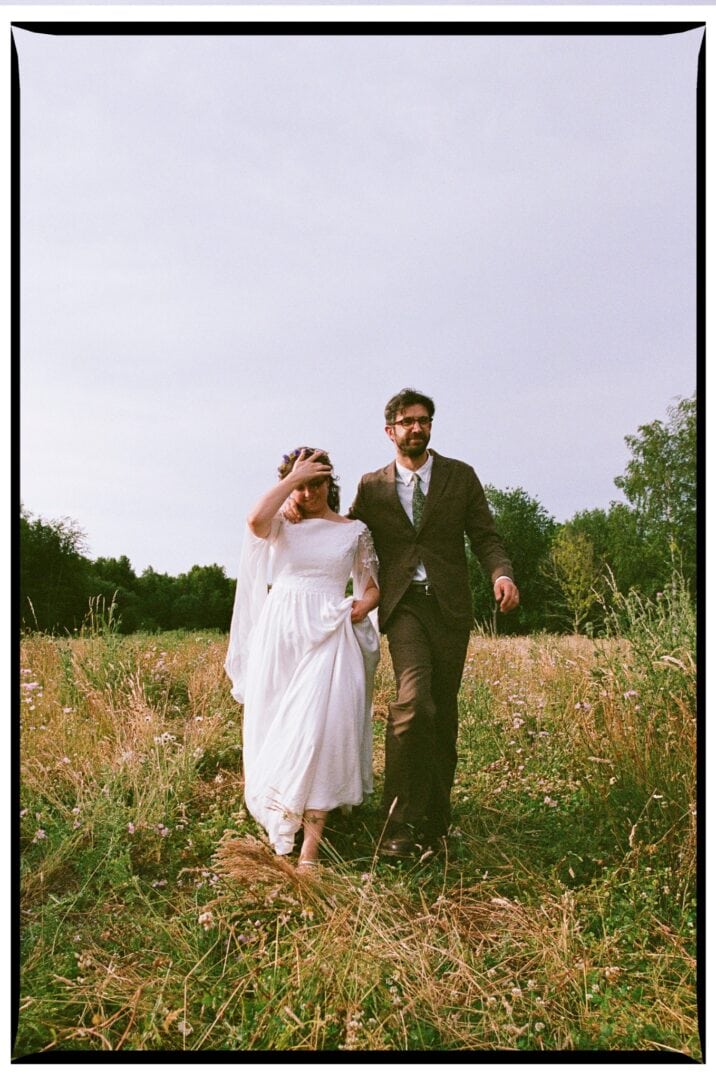 The bride and groom walking towards the camera through long grass