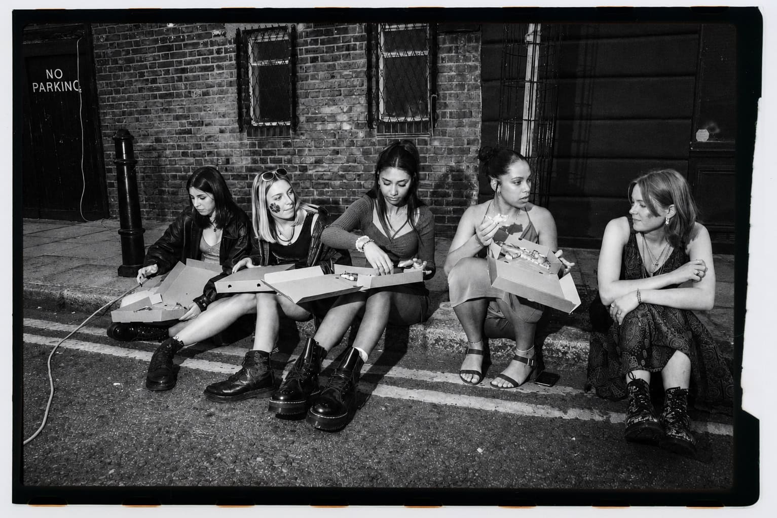 A row of guests sits outside a pizza shop in a black-and-white photograph