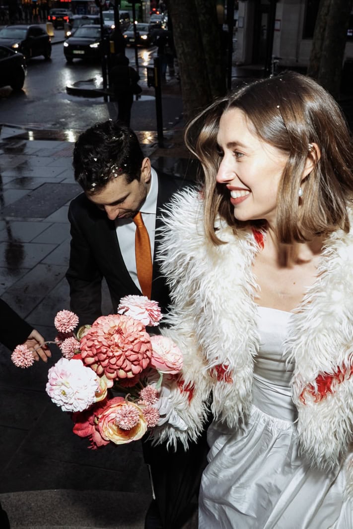 A bride with flowers walks through a London street