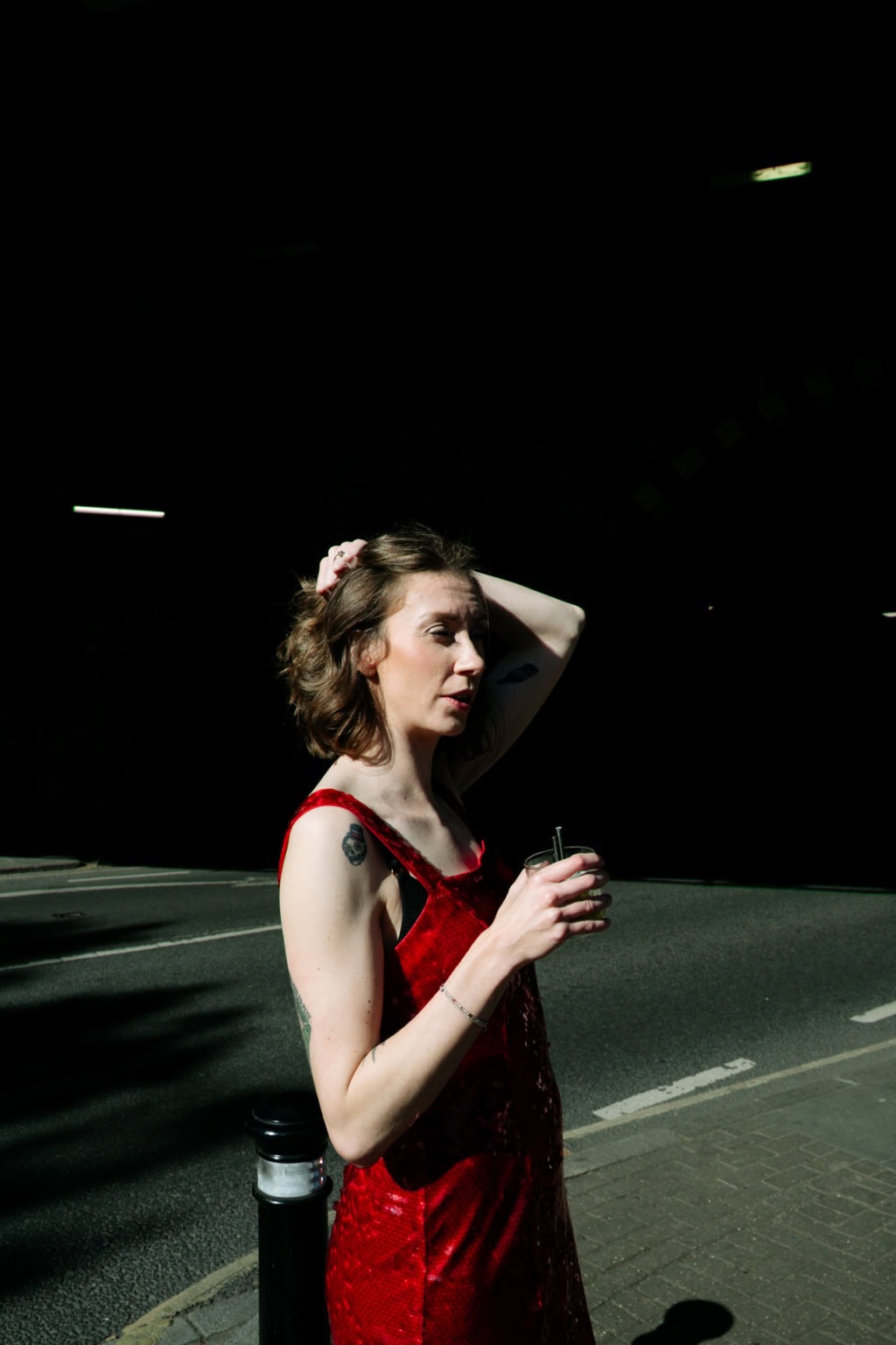 A woman in red holds a drink on a tennis court at night