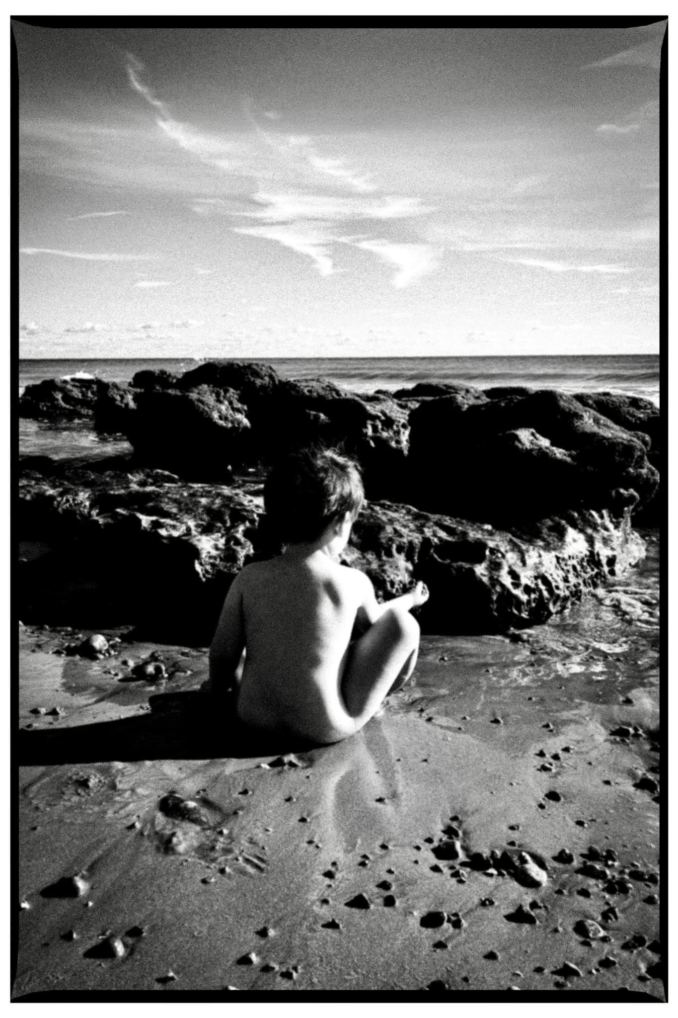 A child seen through a window with seaside houses beyond