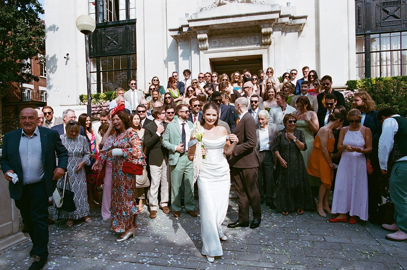 Khalela and Peter walk through confetti on the Town Hall steps, photographed on film