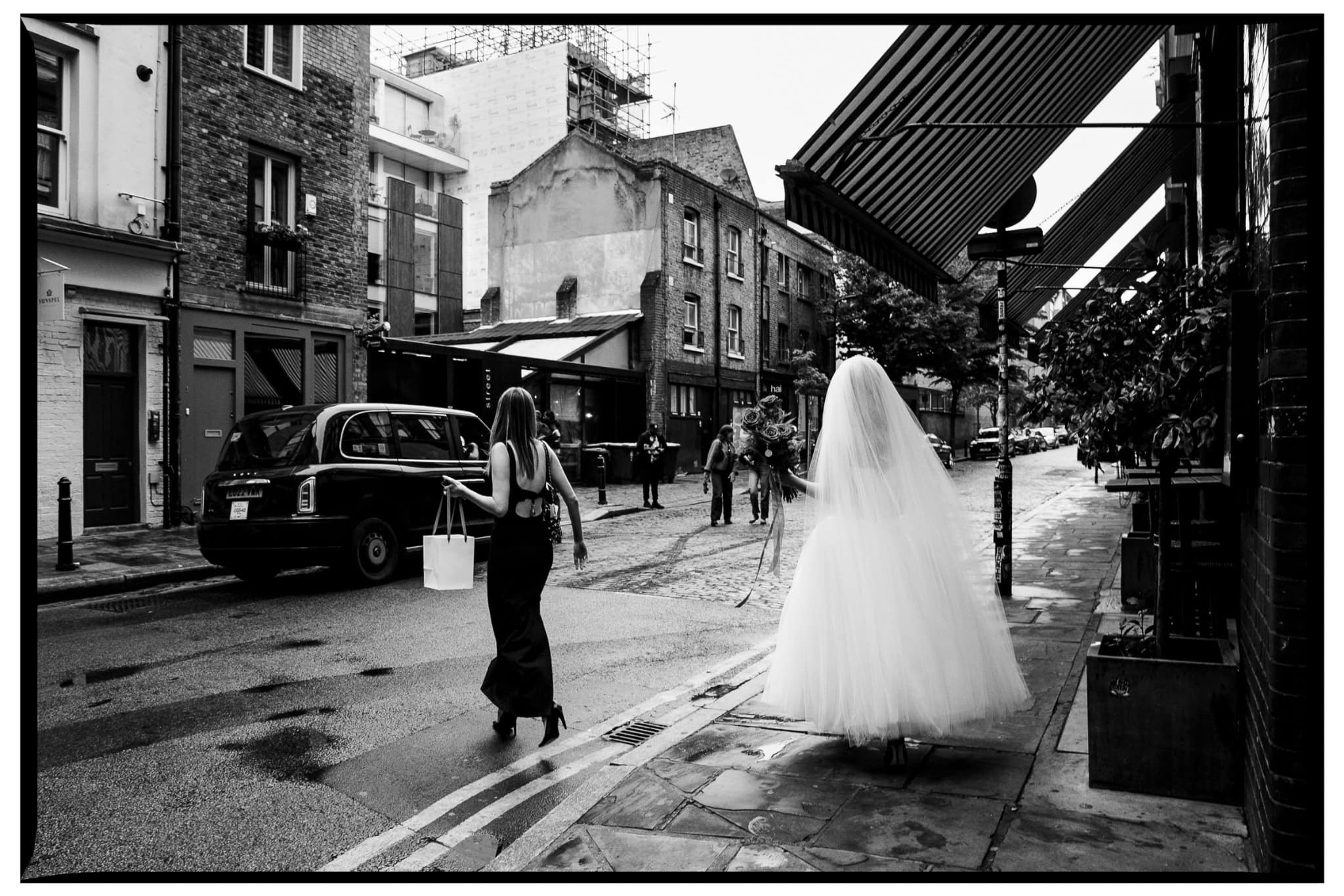 Kate walking along a wet London street in her wedding dress and veil